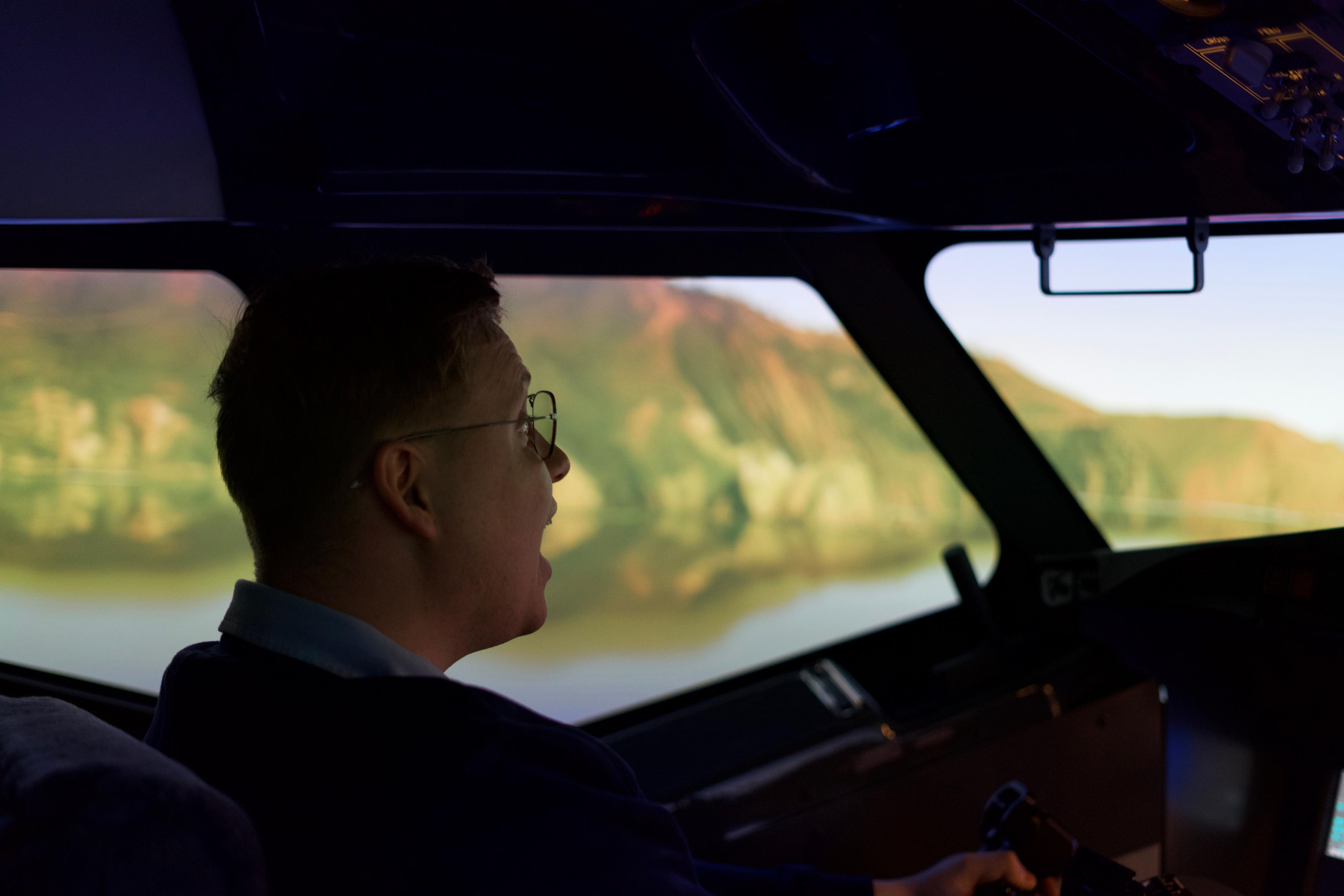 Pilot flying a flight simulator during sunset with scenic landscape outside the cockpit